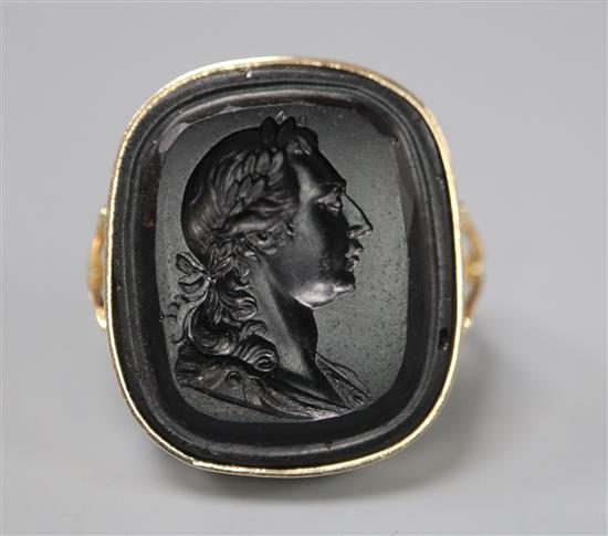A yellow metal and black stone intaglio ring carved with the bust of a gentleman to sinister, size M.